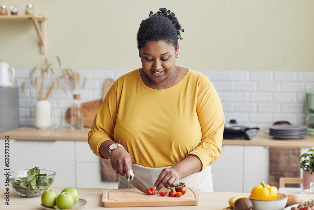 Mulher sorridente cortando vegetais em uma cozinha clara, com expressão de leveza e naturalidade. A cena evoca o prazer de preparar alimentos saudáveis em casa.